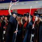 Students in caps and gowns lift their diplomas in celebration during Shenandoah University's 2022 Commencement